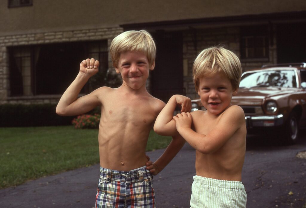 Two young boys (Adam, right, and Karl, left) making muscles in their driveway
