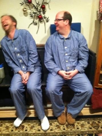 Two adult men wearing matching PJs. Karl, left, is making Adam, right, laugh.
