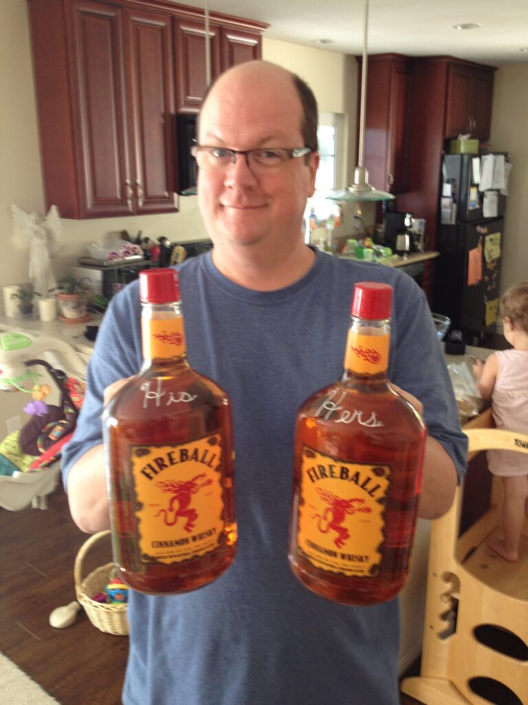 Karl holding two giant "His" and "Hers" bottles of Fireball with a mischevous grin